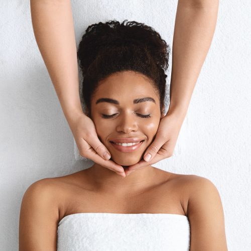 Therapist making lifting facial massage for beautiful black lady