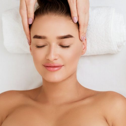 Young woman enjoying face massage and aroma therapy